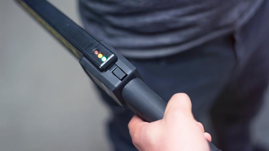 A stock photograph showing a hand-held metal detector used for security checks.