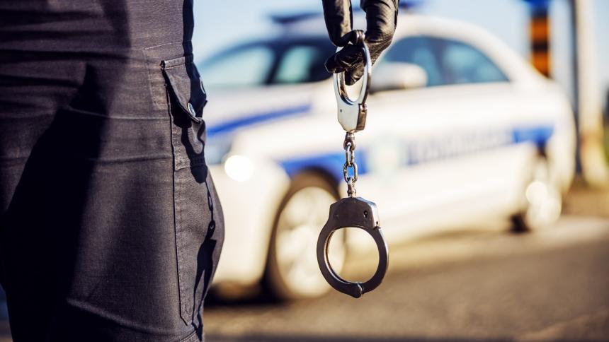 A stock photo showing a police officer holding handcuffs in front of a police car
