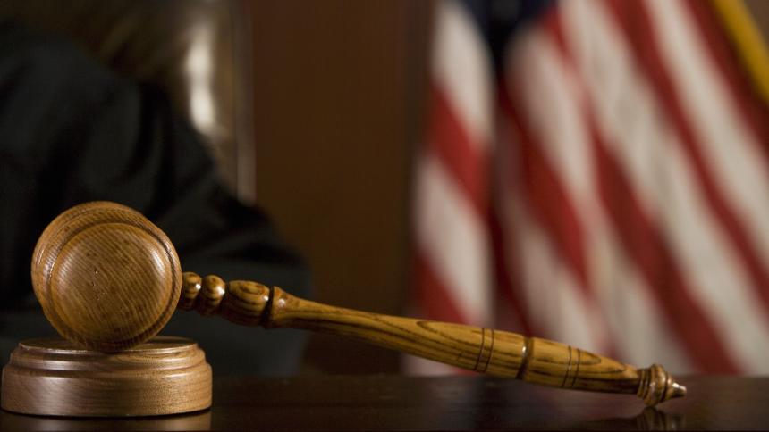 A stock photo of a courtroom gavel with the Flag of the United States in the background.