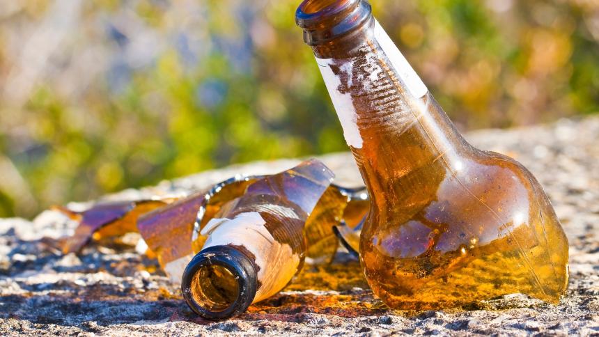 A photograph showing a shattered beer bottle resting on the concrete ground