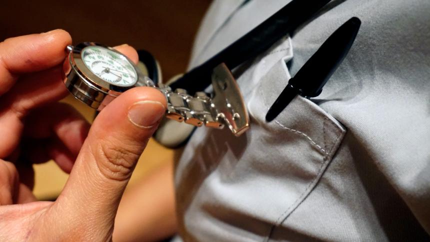 A stock photo showing a nurse checking a fob watch