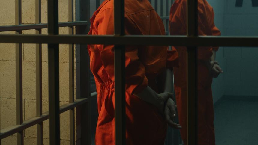 Two prisoners in orange jumpsuits with their hands behind their backs