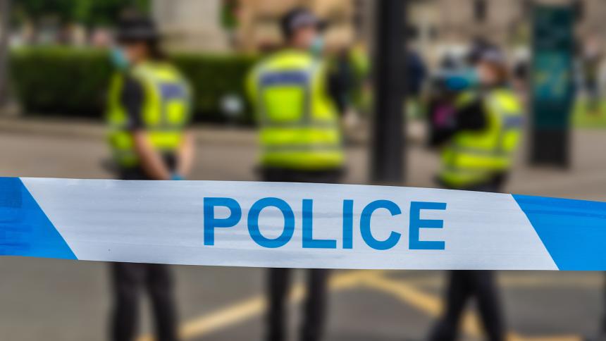 Police tape in front of three British police officers