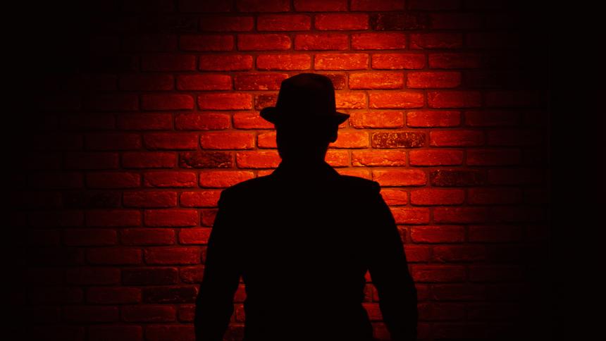 Silhouette of a man wearing a fedora on a red brick background