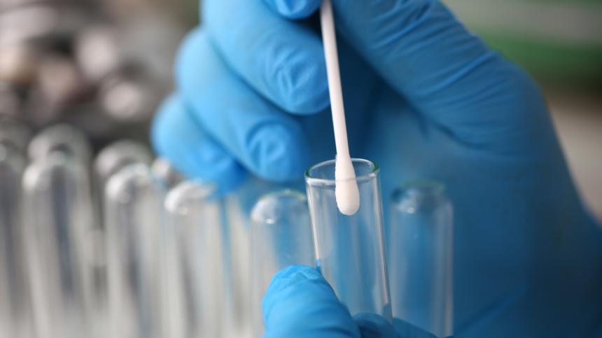 Forensic scientist wearing blue gloves puts a cotton swab inside a test tube