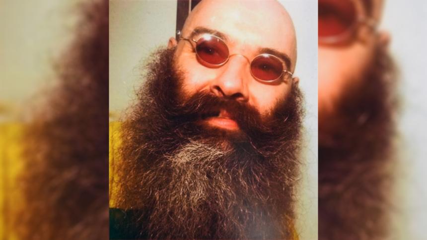 A close up image of Charles Bronson with a large beard and red-tinted sunglasses