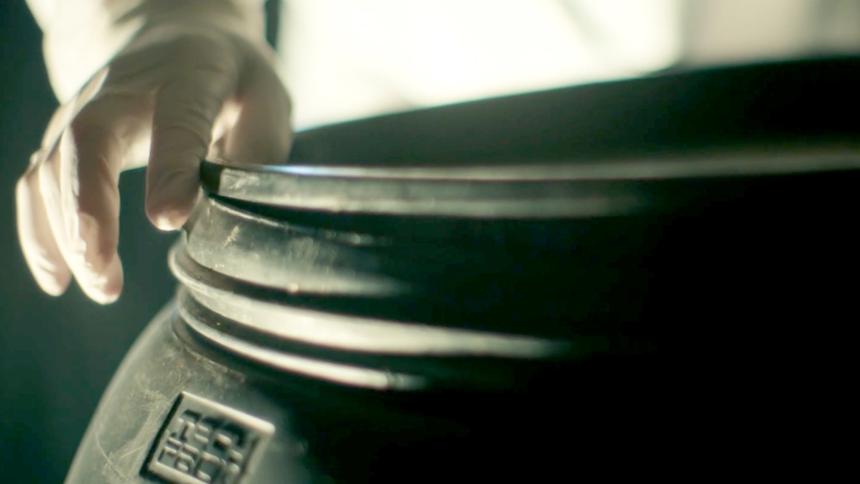 A person with a latex glove on sealing the lid of a large plastic barrel