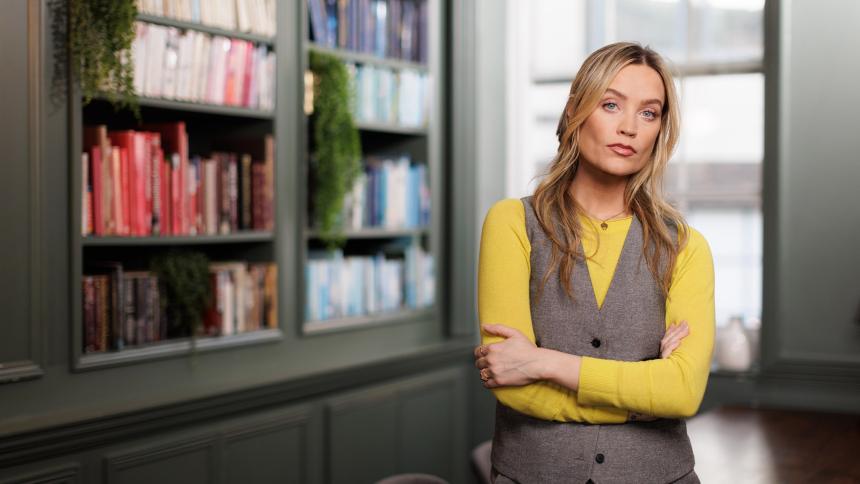 Laura Whitmore standing with her arms crossed in front of a large bookcase