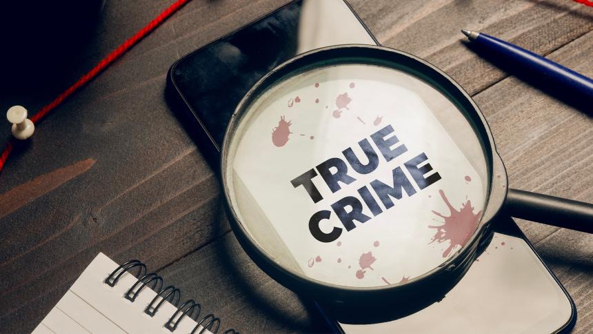 A magnifying glass lying on a smartphone with the words 'True Crime' written on the screen
