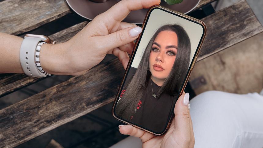 A woman holding a smartphone with an image of True Crime Caitlyn on