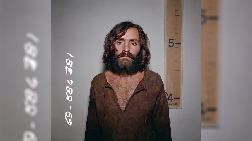 Charles Manson mugshot in front of a height chart that shows him to be a few inches taller than five foot