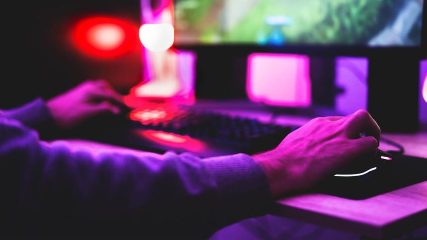 Someone using a PC set up to play an online game with purple lights shining on them