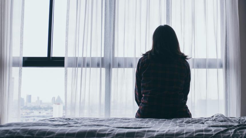 A woman sitting on a bed looking out of the window